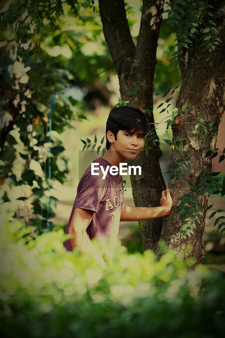 Portrait of teenage boy standing by trees in yard