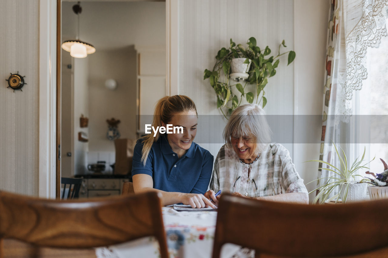 Smiling female caregiver assisting senior woman doing puzzle at home