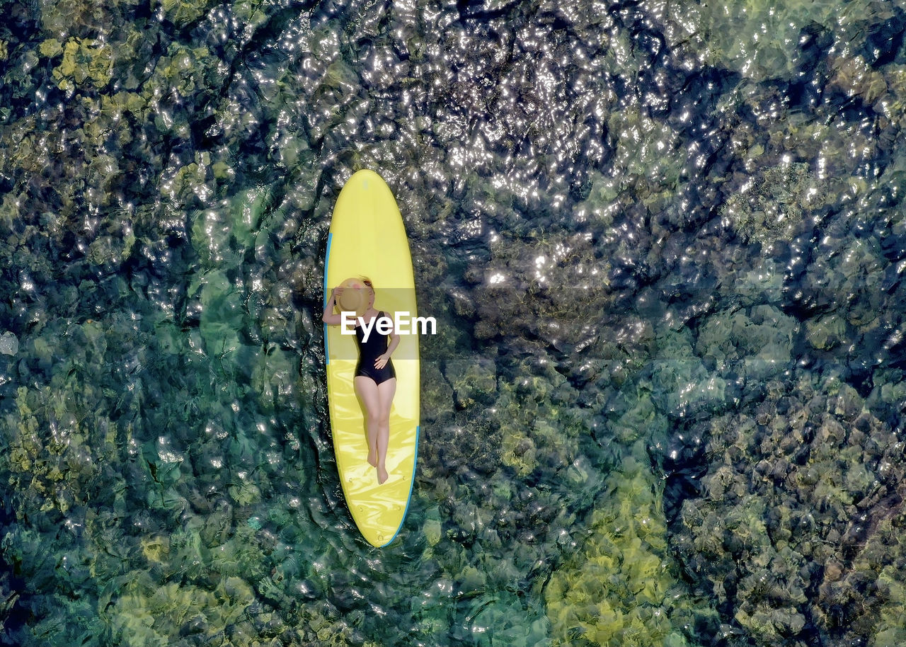 High angle view of a young woman floating on a surfboard in the middle of the sea