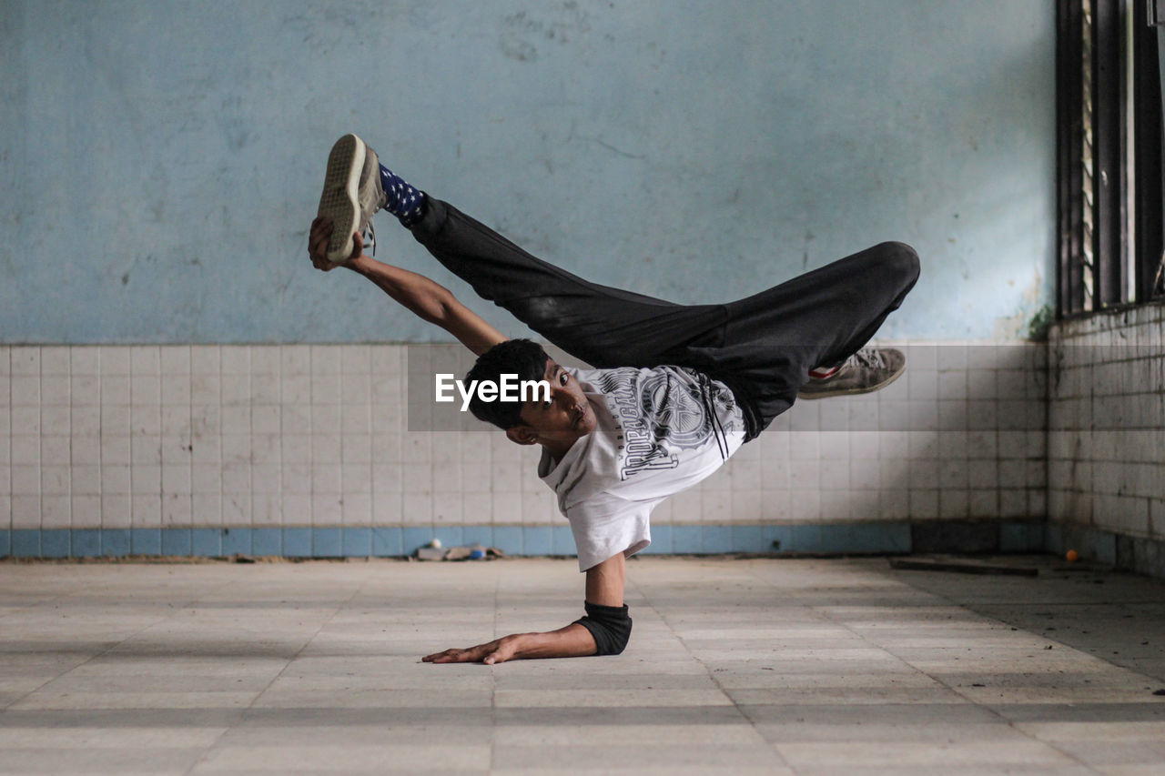 Portrait of young man performing stunts in room against wall