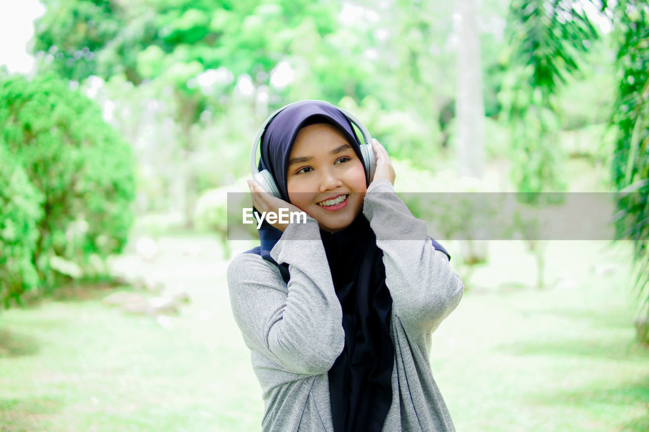 Beautiful young asian muslim woman listening to music with headphones in a park