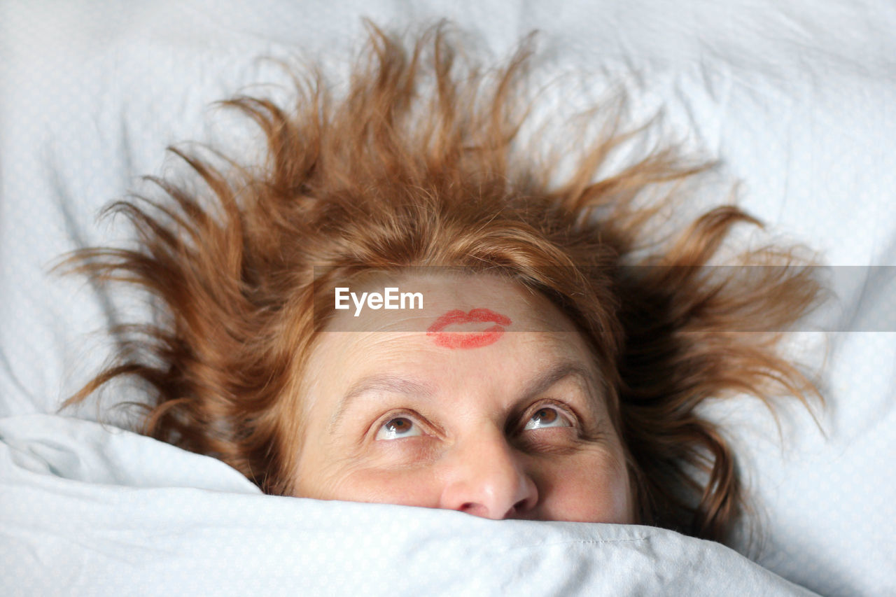 Woman with lipstick mark on head sleeping on bed