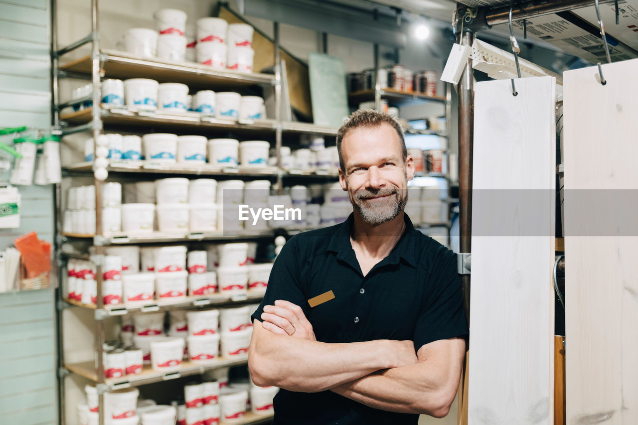 Portrait of smiling salesman with arms crossed standing in store