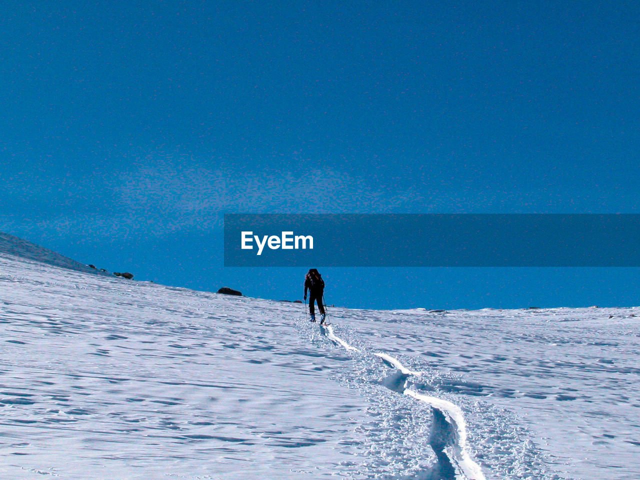 PERSON WALKING ON SNOWCAPPED MOUNTAIN AGAINST BLUE SKY