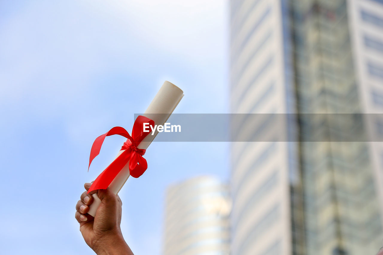 Low angle view of hand holding rolled paper against building in city