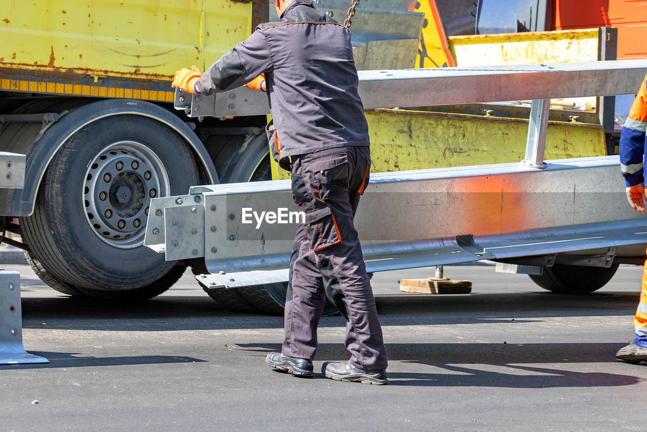 transportation, mode of transportation, vehicle, adult, asphalt, occupation, land vehicle, motor vehicle, men, day, working, road, full length, one person, person, clothing, city, standing, car, industry, transport, outdoors, footwear, wheel