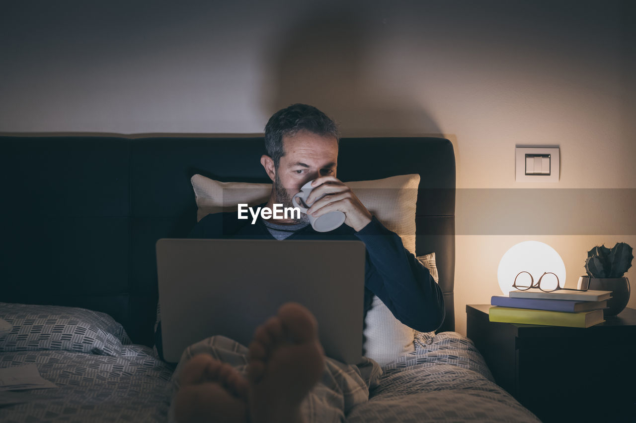 Man works with laptop lying on bed. male home working remote office sitting in bedroom use devices