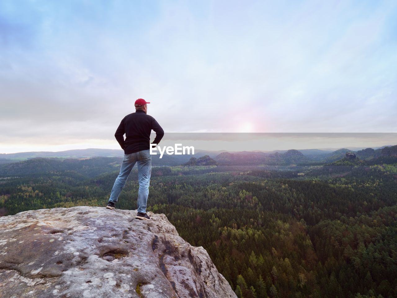 Man in jeans black outdoor sweatshirt and red cap. melancholy misty day in sandstone mountains
