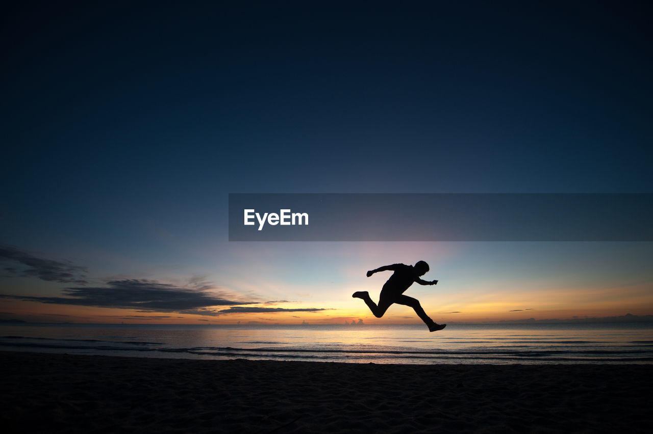 Silhouette man jumping at beach against sky during sunset