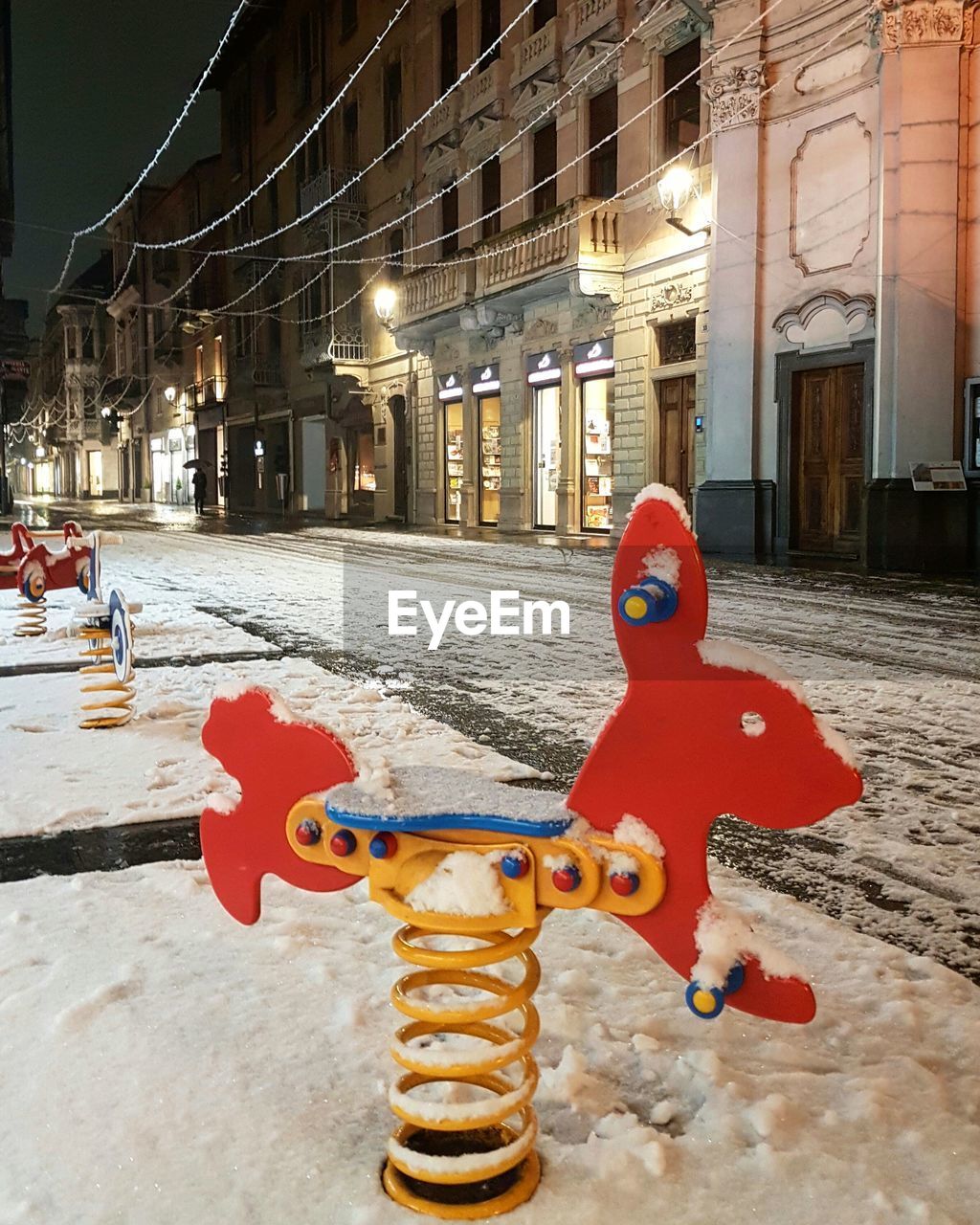 Playground covered with snow in the empty main street of alba at night, piedmont, italy


