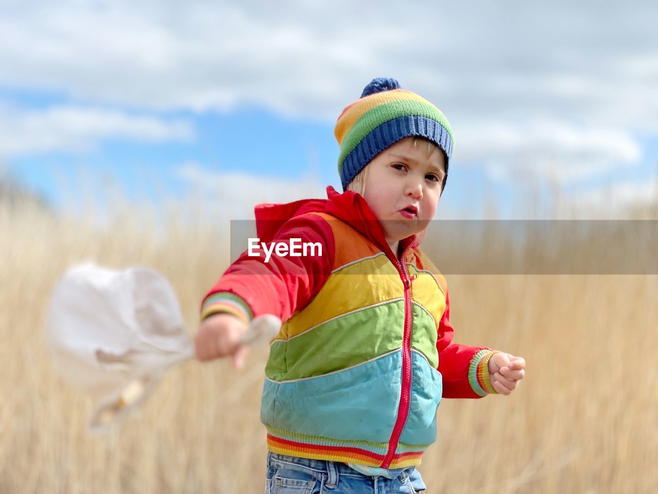 Boy wearing hat standing on field against sky