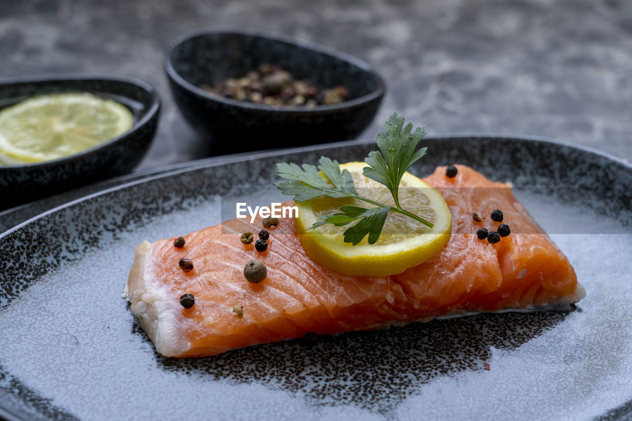 Row salmon fish fillet uncooked with different spices and lemon slice served on plate.