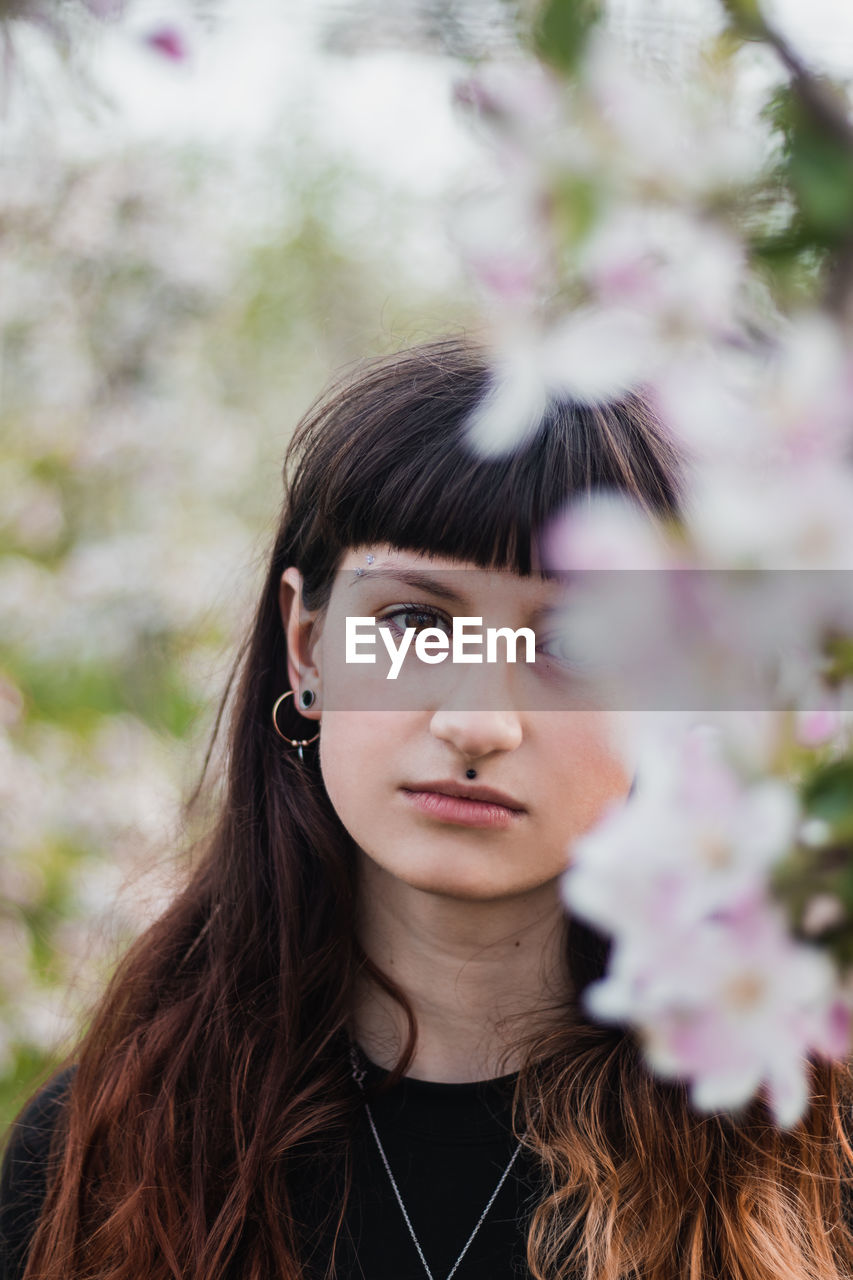 Candid portrait of a beautiful brown-haired woman with facial piercings in blossoming apple orchard