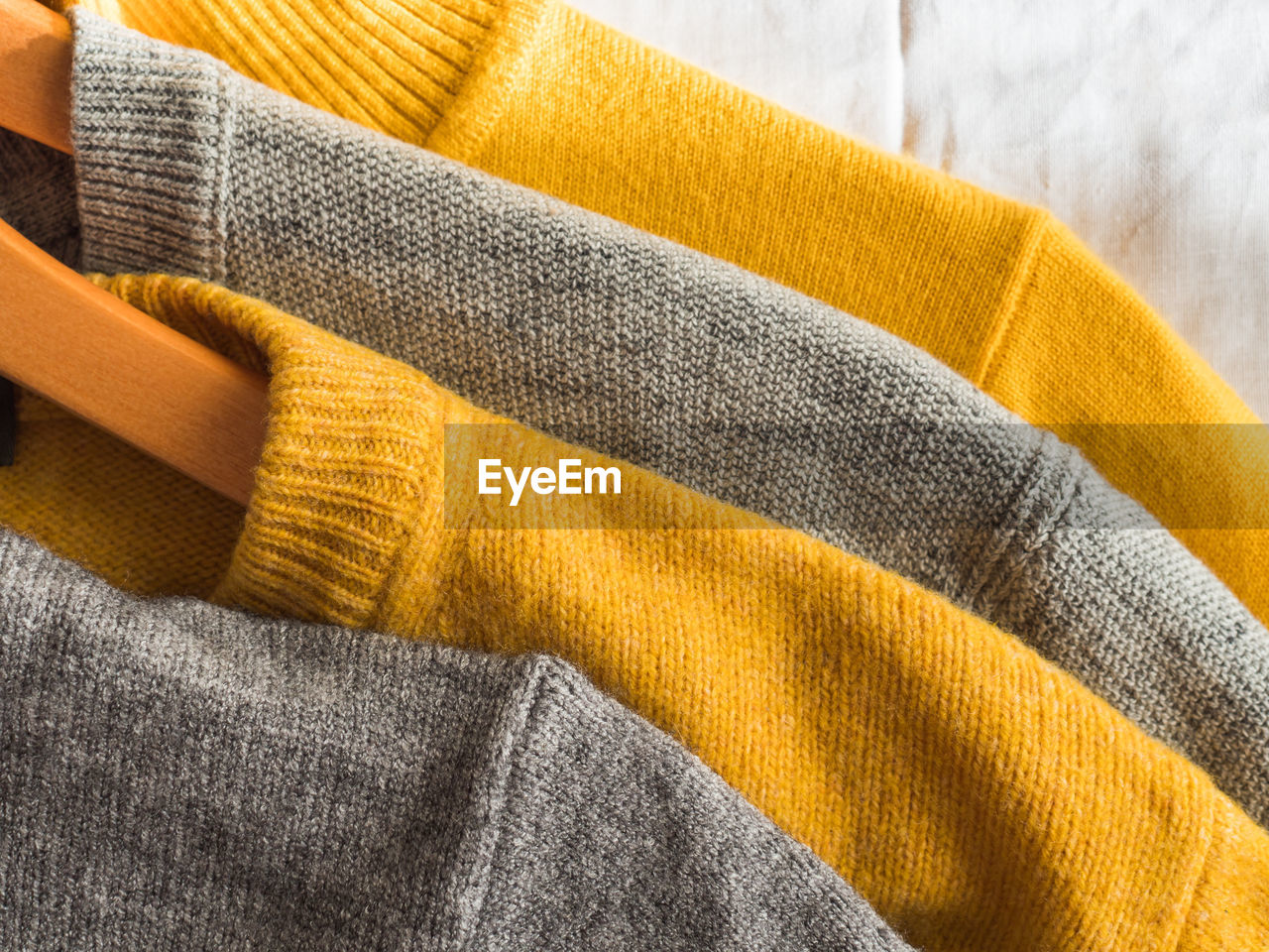 Yellow illuminated color and gray winter sweaters on wooden hangers. trendy fashion cozy clothes.