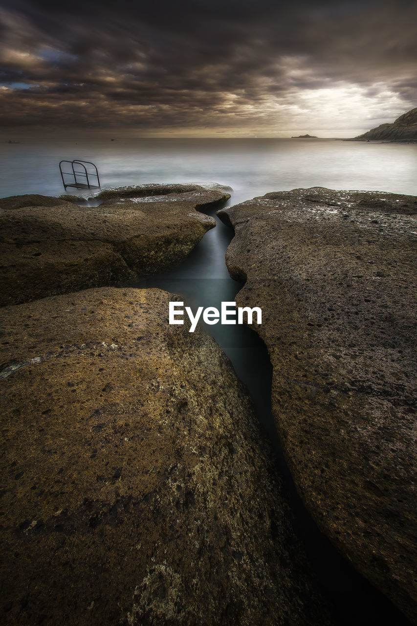 Scenic view of rock formation in sea against sky during sunset
