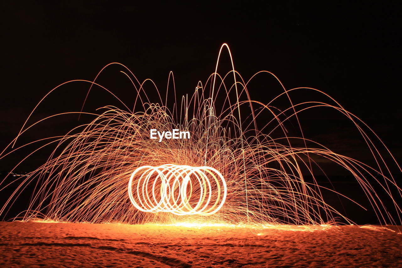 Illuminated wire wool at beach against sky