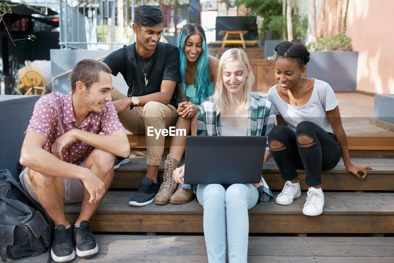 Cheerful friends looking at laptop in campus