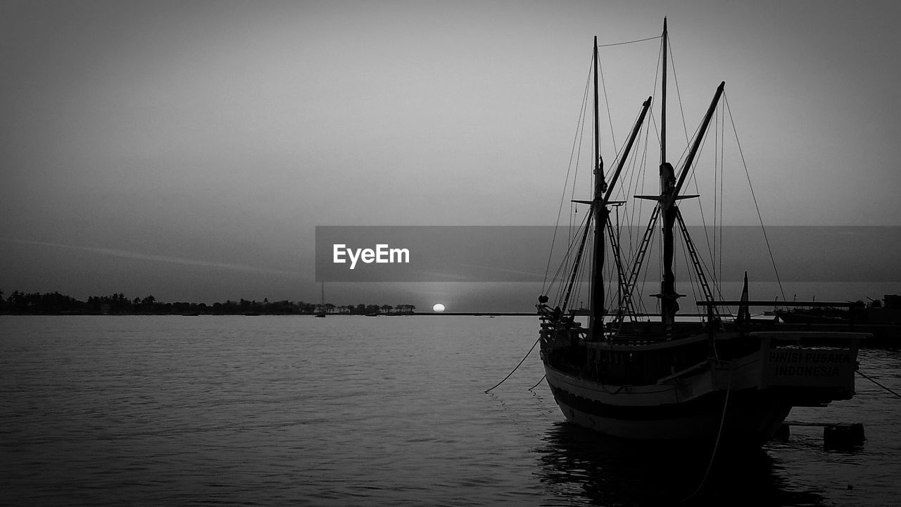 Sailboat moored in sea against clear sky during sunset