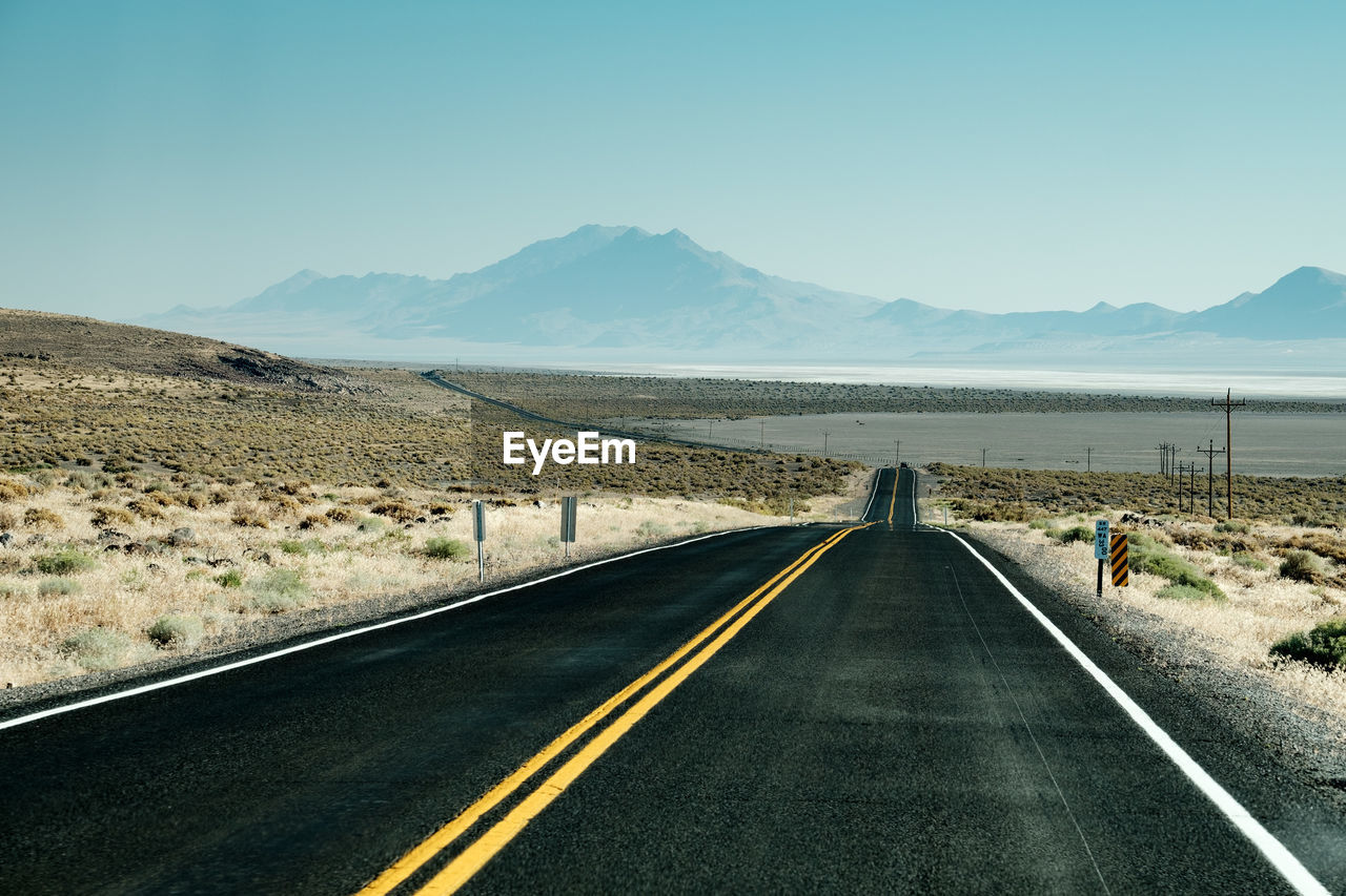 REAR VIEW OF MAN ON ROAD AGAINST MOUNTAIN RANGE