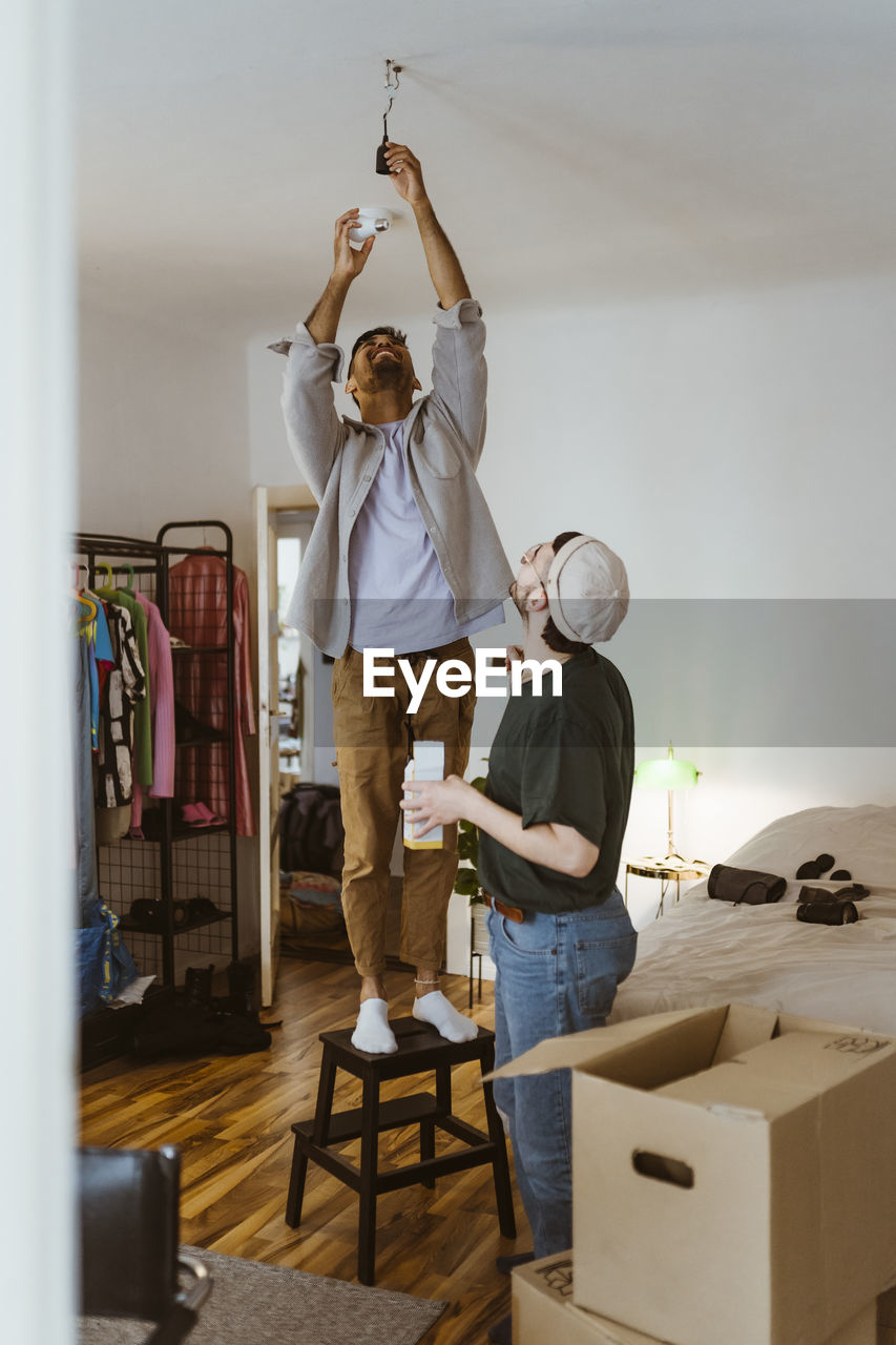 Man installing bulb while standing on stool with boyfriend in living room at home