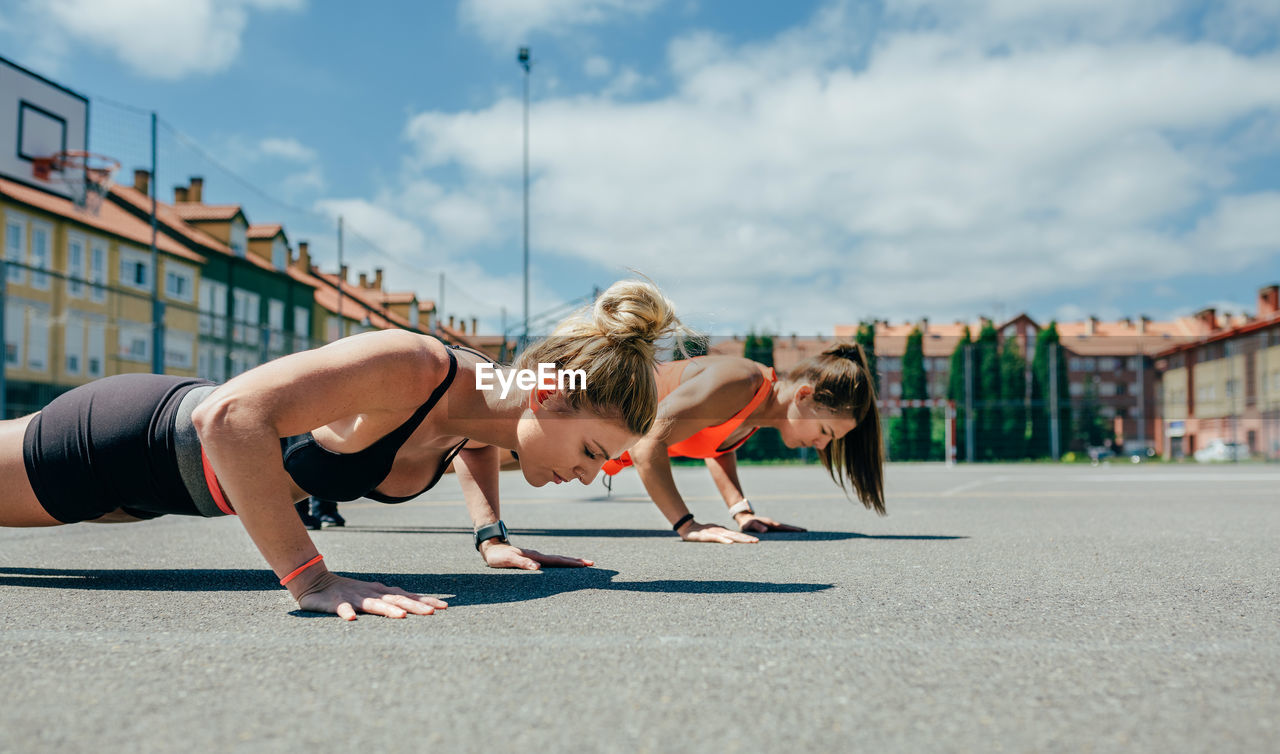 Women doing push-ups on land in city against sky