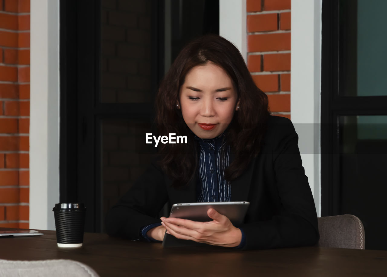 YOUNG WOMAN USING SMART PHONE WHILE STANDING ON LAPTOP