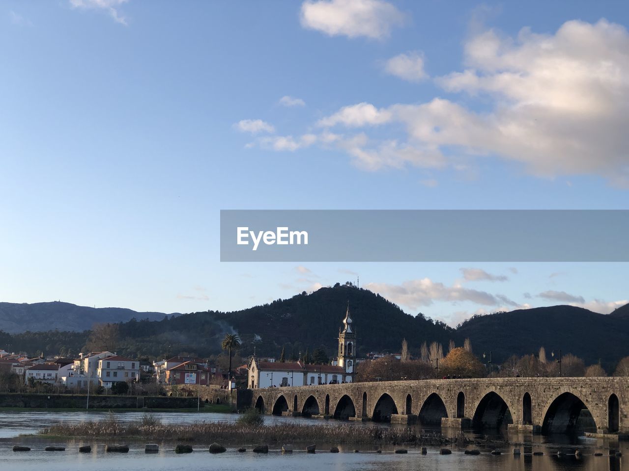 Arch bridge over river by buildings against sky