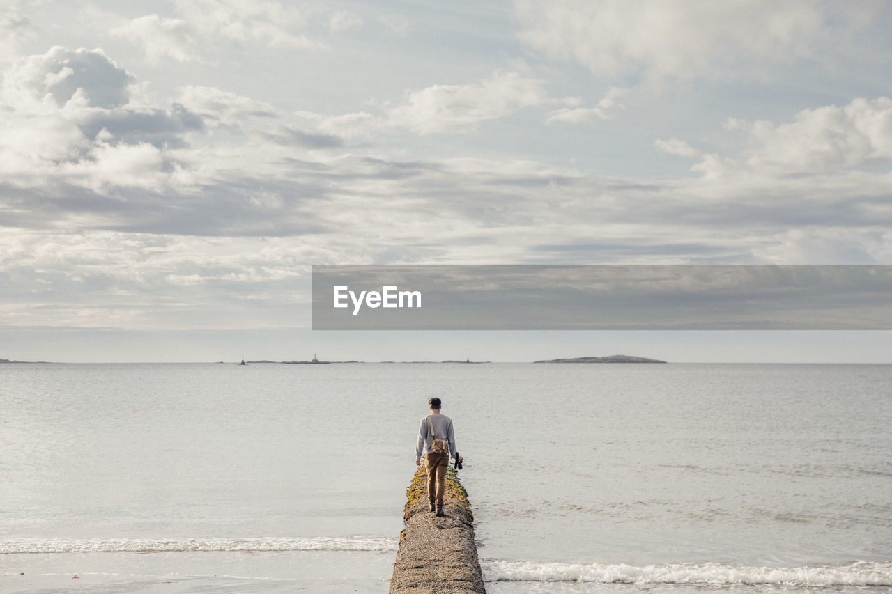 Rear view of man walking on pier in sea against sky