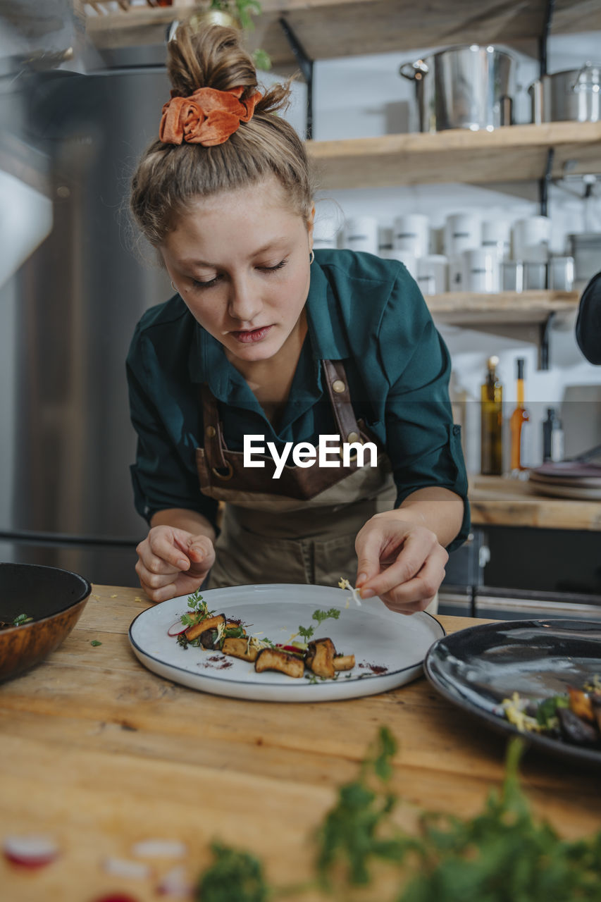 Young female chef garnishing dish while standing in kitchen