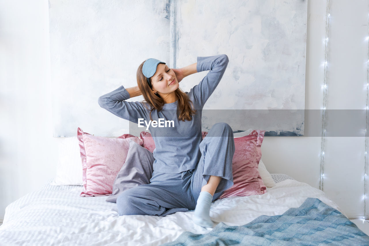 Happy healthy, beautiful young woman wearing sleep mask and blue pajamas, awake