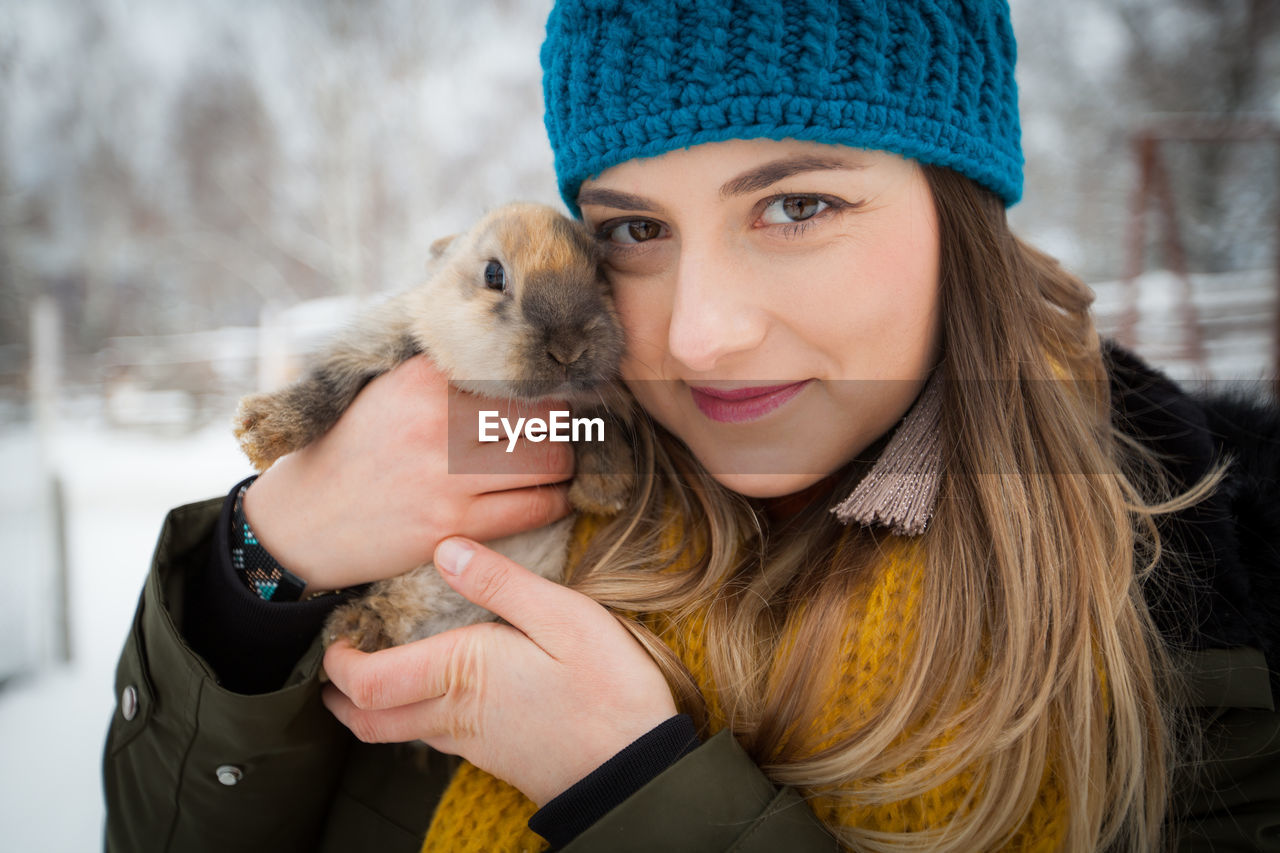 Close-up portrait of woman holding rabbit while standing on field during winter