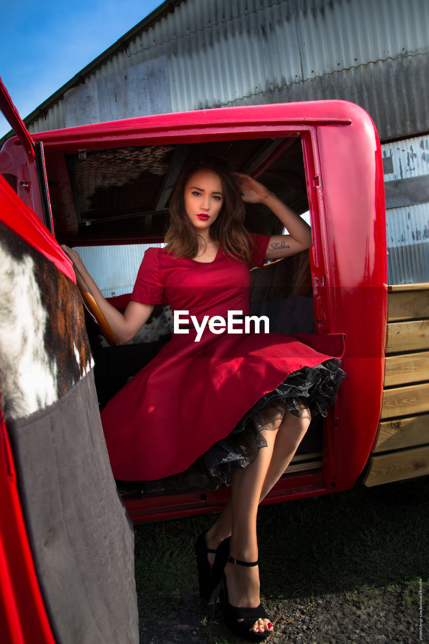 Portrait of beautiful young woman in red dress sitting in pick-up truck