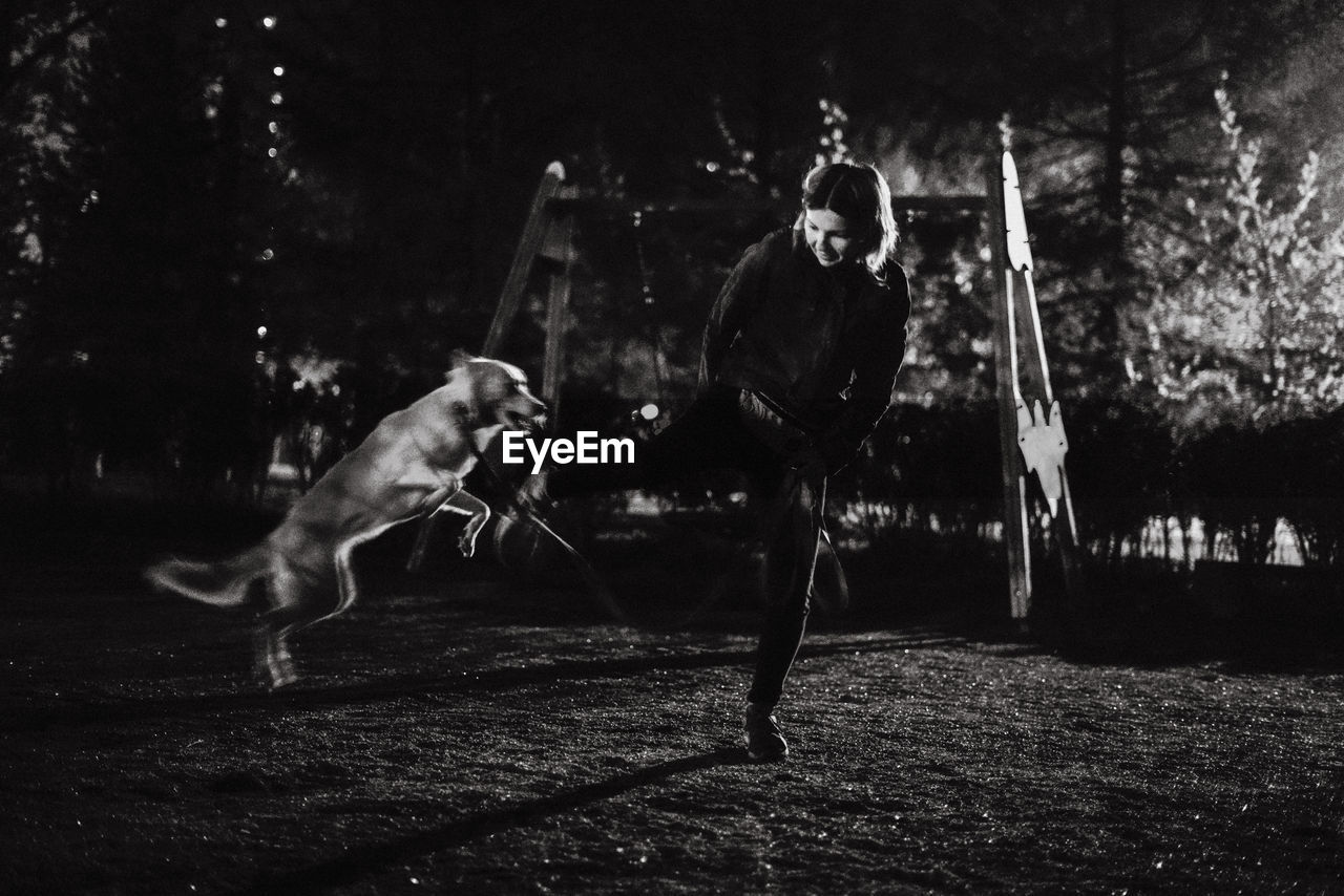 Young woman playing with dog in park at night