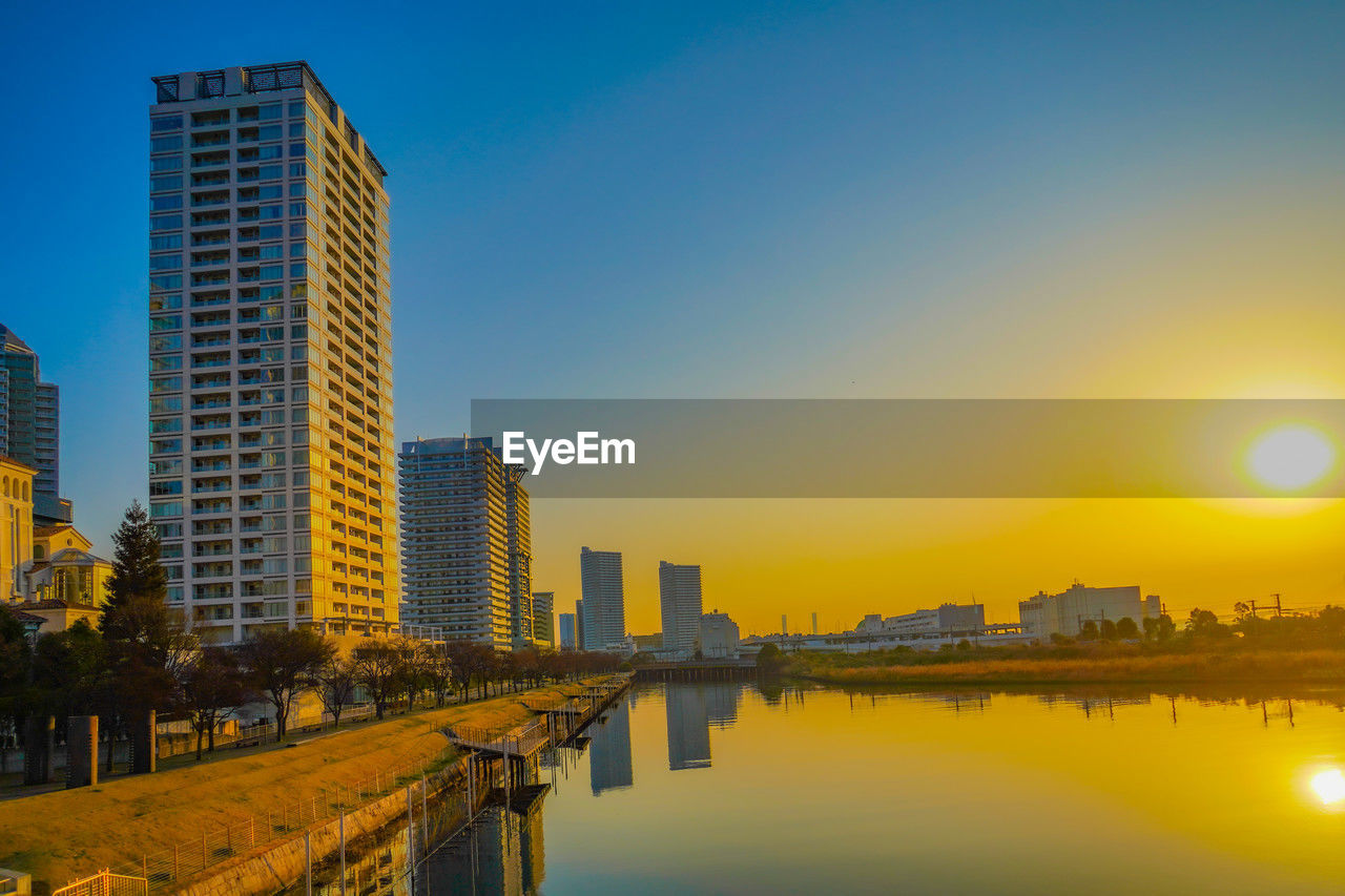 reflection of buildings in city against sky during sunset