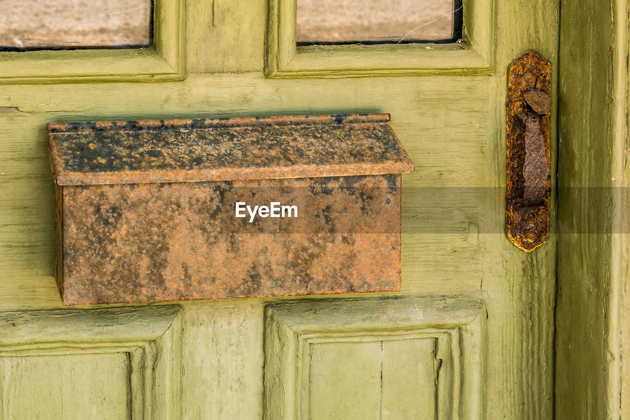 Green wooden door with mottled rusted mailbox