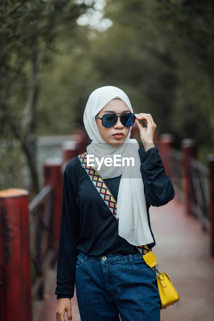 Young woman wearing sunglasses while standing on footpath