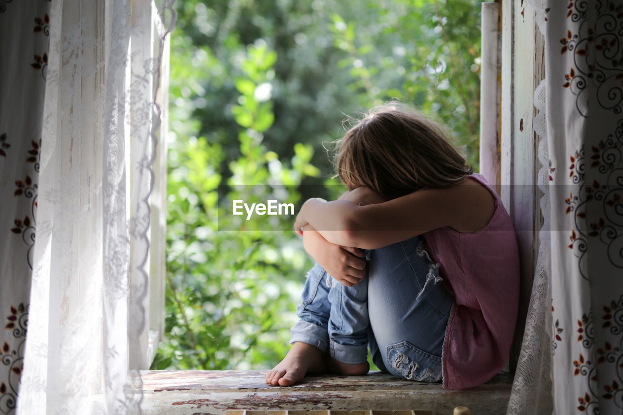 Child girl on the window, the concept of sadness and loneliness, the problems of childhood