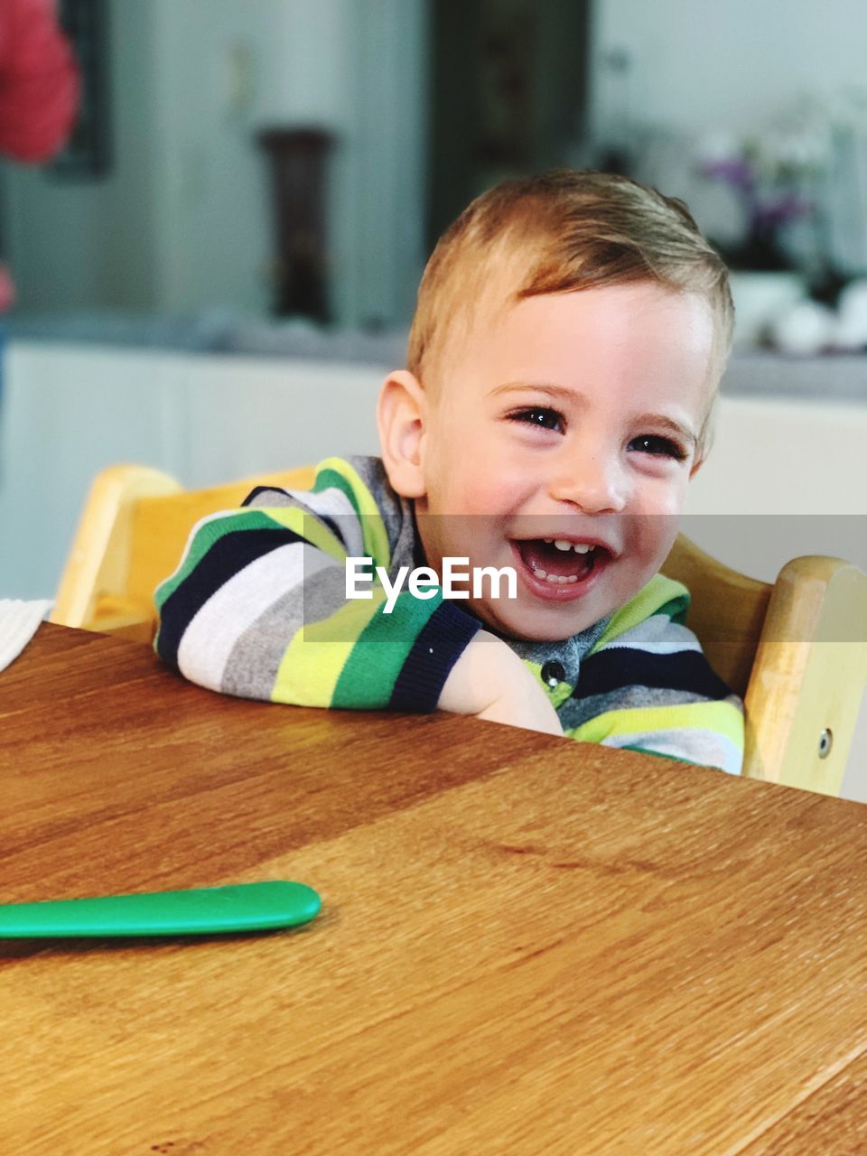 Cheerful baby boy looking away while sitting at table in home