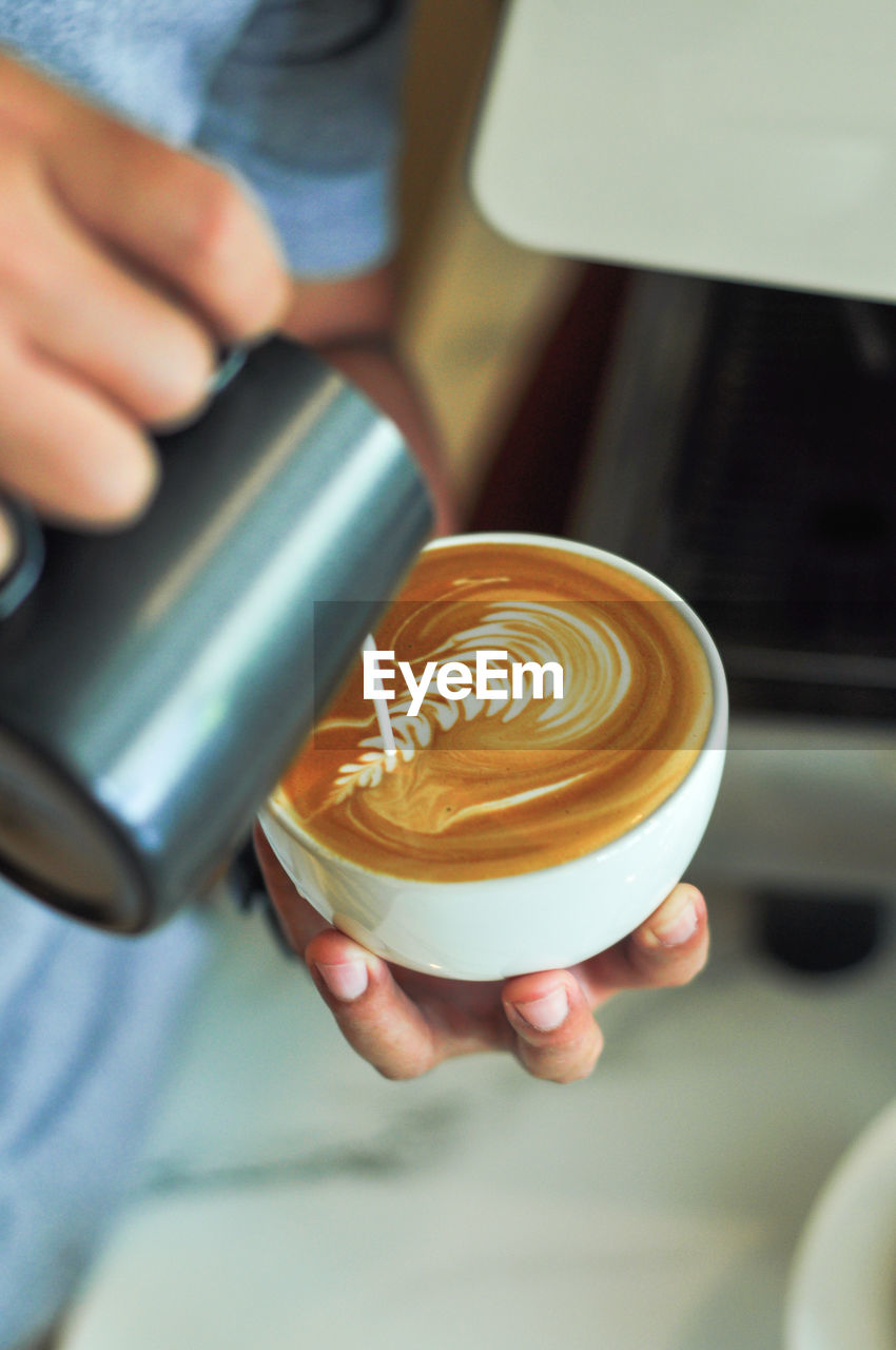 CROPPED IMAGE OF HAND HOLDING COFFEE CUP WITH CAPPUCCINO