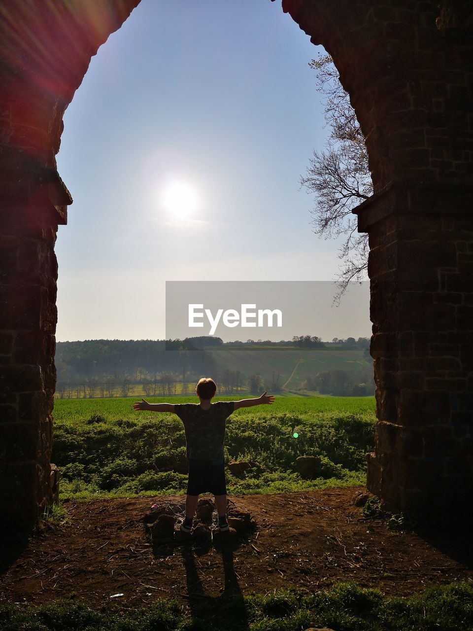 Rear view of boy with arms outstretched standing on land against sky