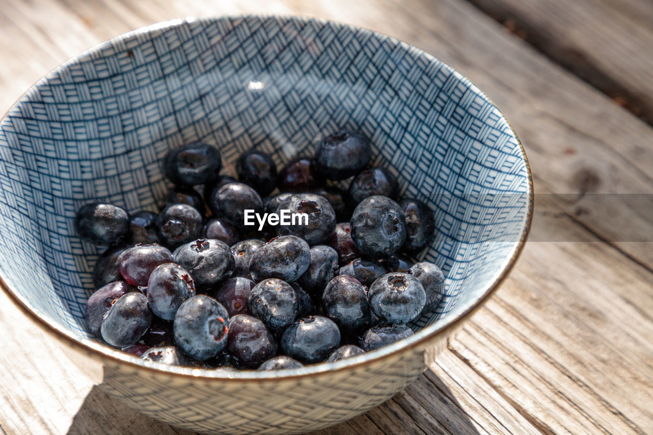 Organic blueberries in a blue and white bowl on the rustic wood background of an old farm table