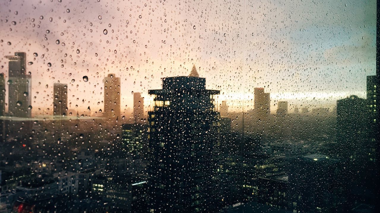 Waterdrops on glass against silhouette buildings