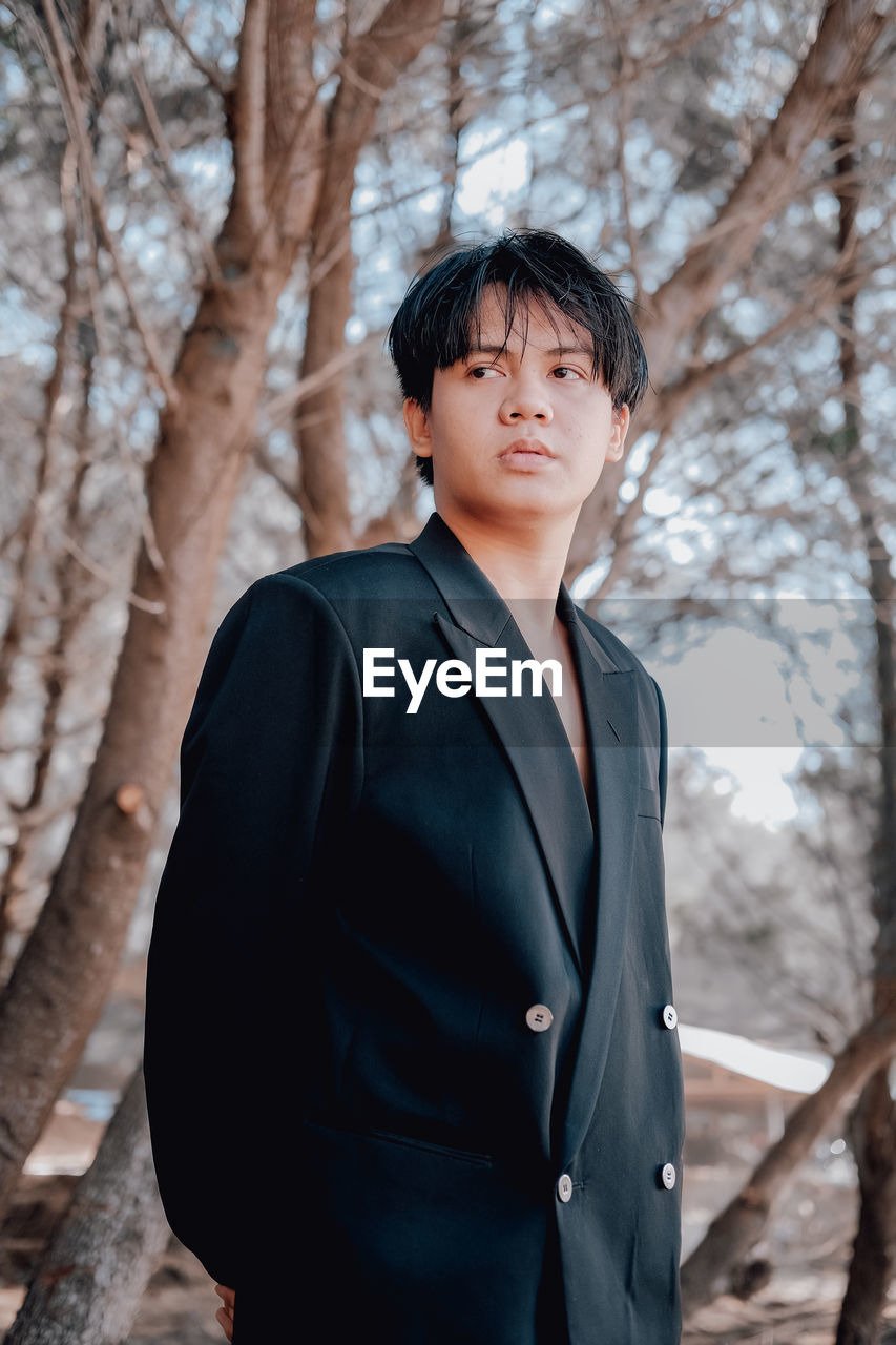 Young man standing by bare trees in forest