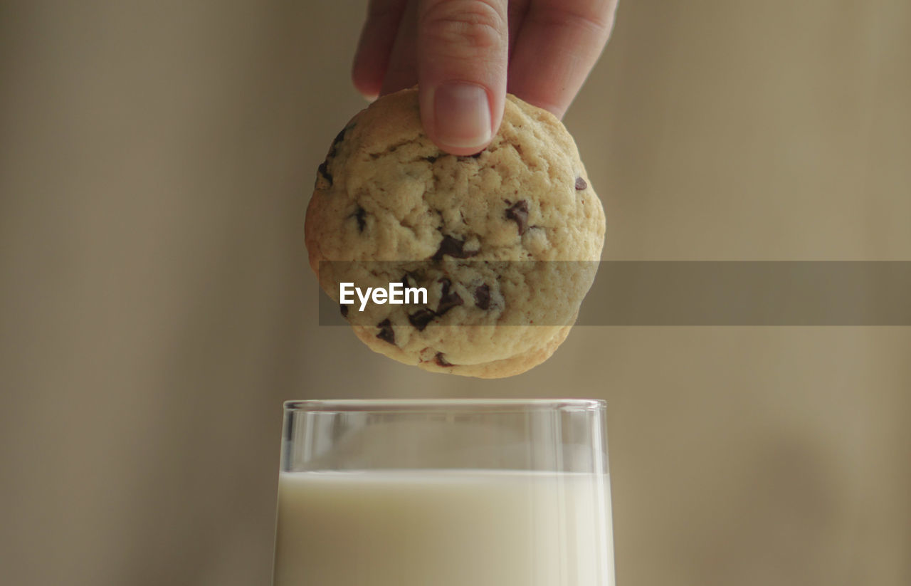 Close-up of hand holding cookies over milk