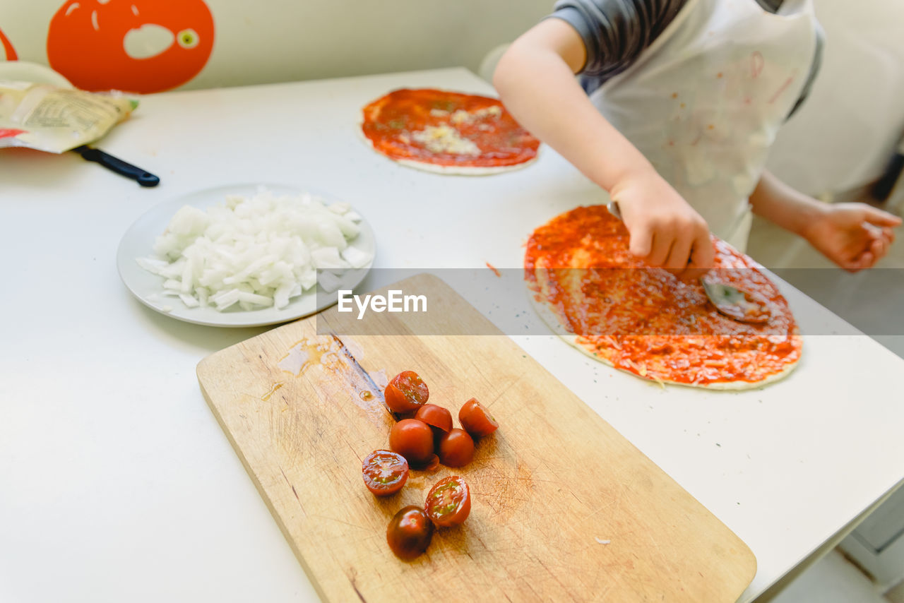 Midsection of boy making pizza on table at home