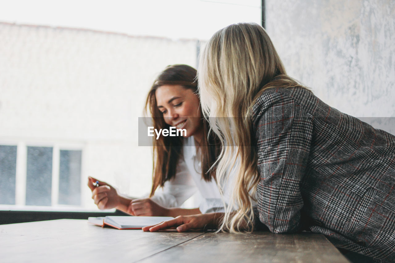 YOUNG WOMAN USING PHONE WHILE SITTING ON TABLE AT HOME