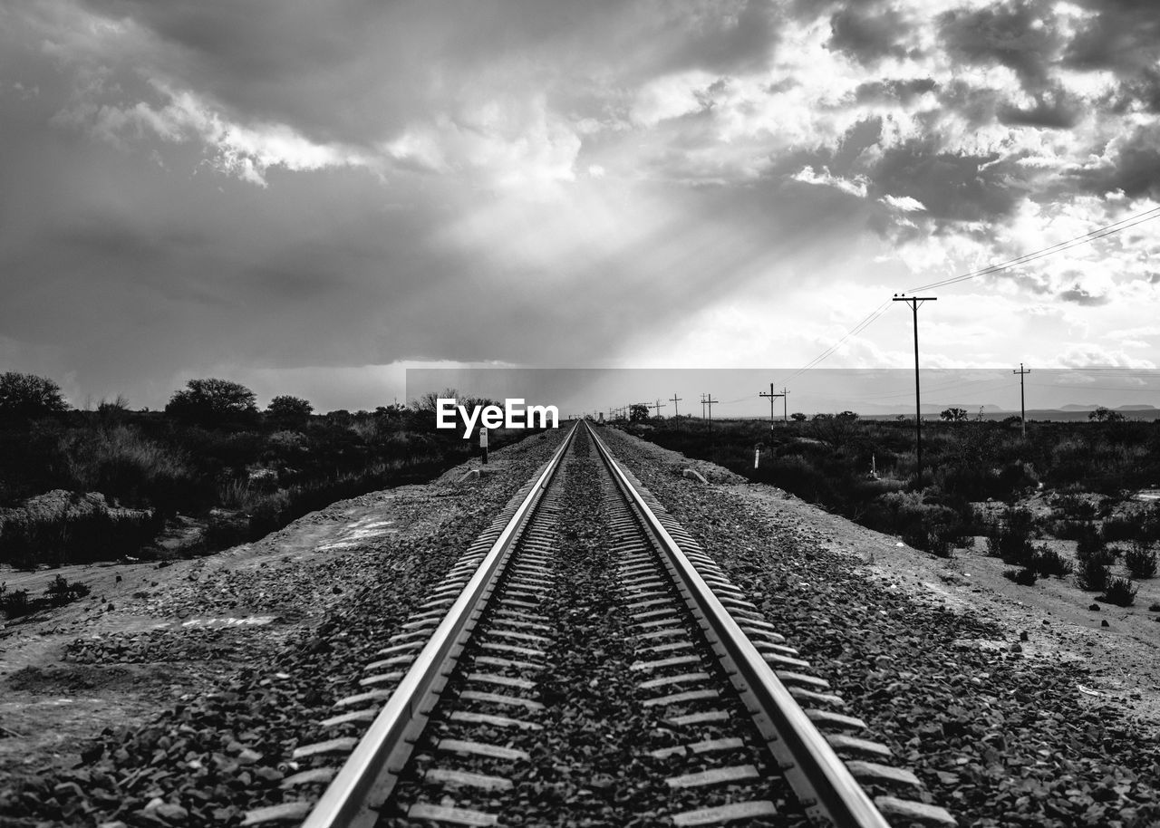 Railroad track on field against cloudy sky