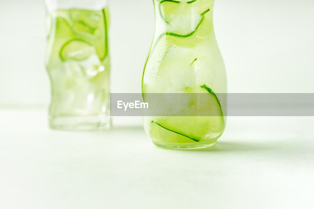 Cucumber infused water in glass jar and highball glass, closeup view, with copy space.