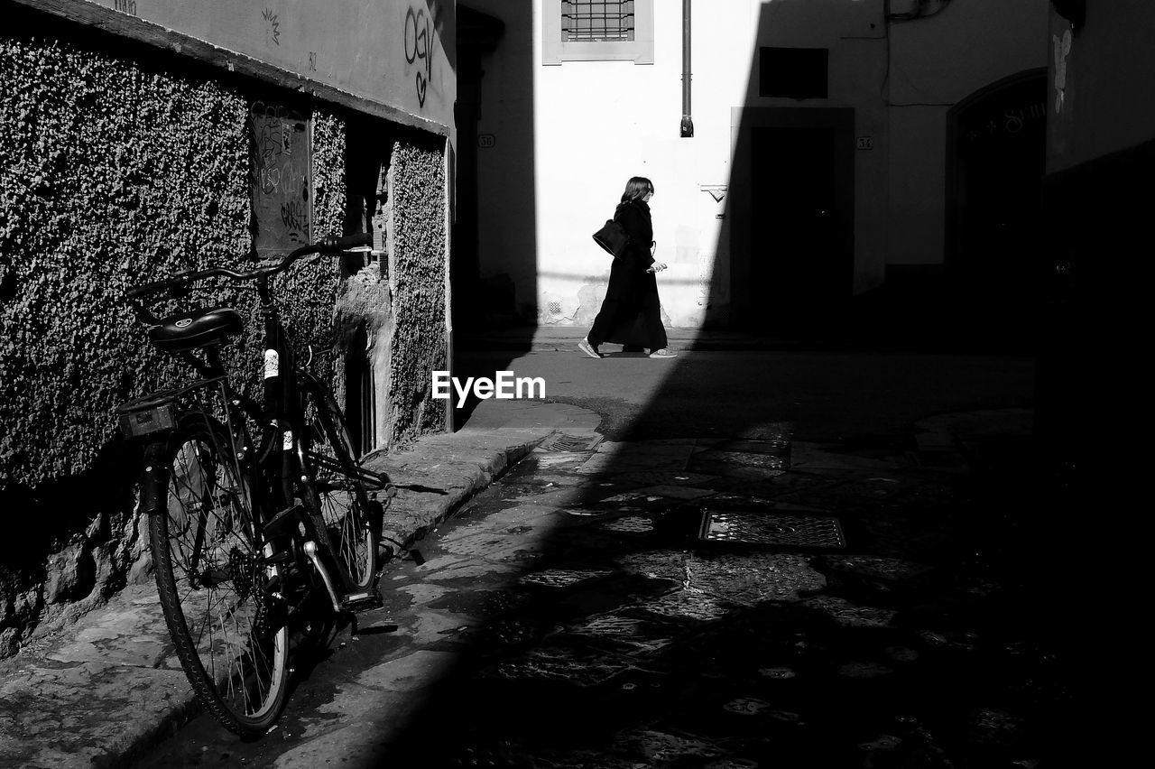 REAR VIEW OF MAN WALKING IN ALLEY AMIDST BUILDINGS