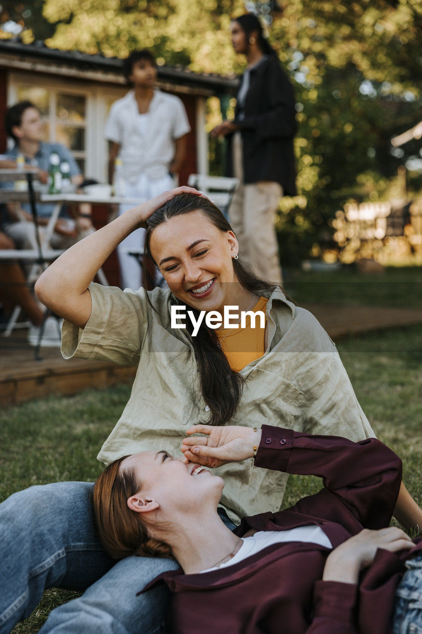 Happy woman lying down on lap of female friend sitting on grass in back yard